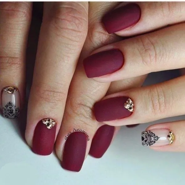 Бордовий матовий максималізм на овальних нігтях: святковий дизайн із золотом та стразами